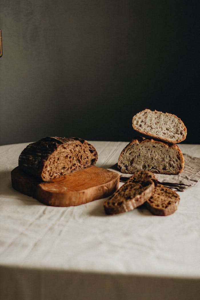 Delicious homemade cut loaves of black and white bread placed on white table with wooden cutting board on gray background in light studio